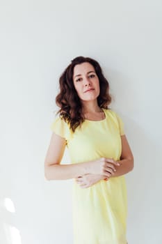 brunette woman in a yellow dress stands in a bright room