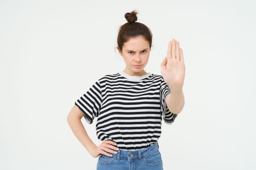 Image of woman frowning, showing one palm, stop gesture, disapprove and reject something, makes prohibit gesture, standing over white background.