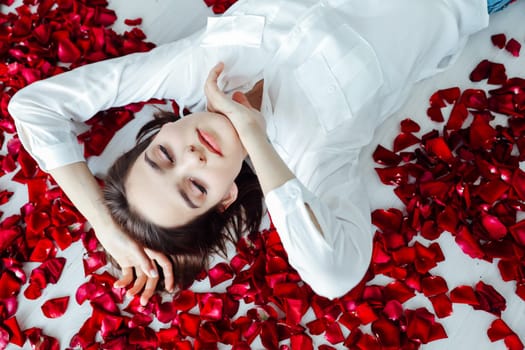 woman lies in red rose petals on the floor of the room