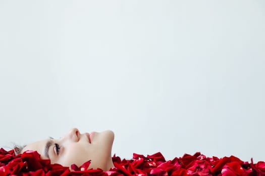 the face of woman in red rose petals on a light background