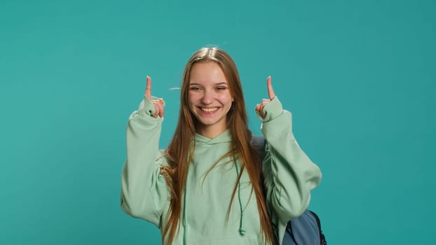 Upbeat woman pointing with finger in all directions, doing advertising, talking with audience. Young teenager doing presentation, showing copy text, studio backdrop, camera A