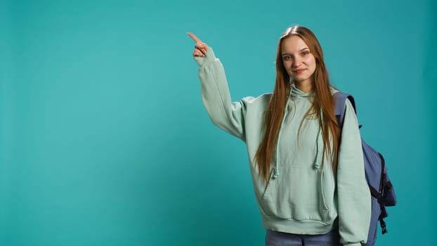 Portrait of cheerful person pointing finger towards empty space, doing advertising. Happy lady doing presentation, showing copy text, isolated over studio background, camera B