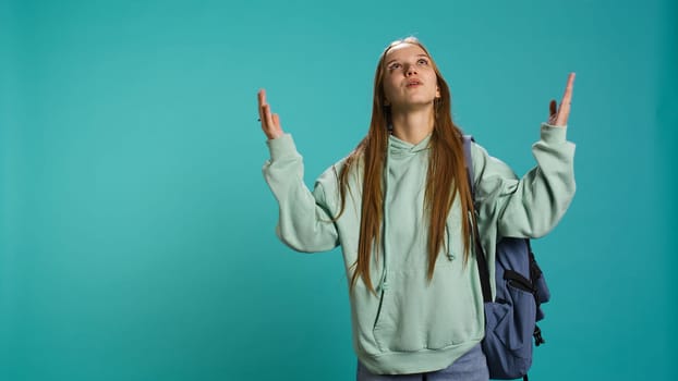 Pious woman looking up towards sky, waiting for sign from god. Spiritual girl doing worship hand gesturing, spreading arms, hoping for miracle, studio background, camera B