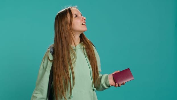 Joyous young traveler holding passport, going on vacation, looking around after arriving in new place. Happy girl travelling, sightseeing, visiting attractions, studio background, camera A