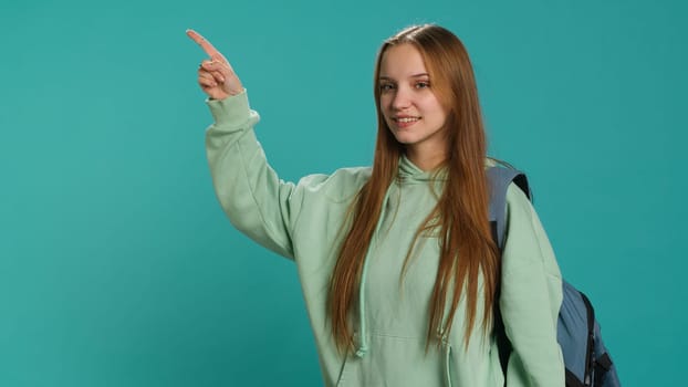 Radiant woman pointing finger towards empty space doing advertising, talking with audience. Smiling young girl doing presentation, showing copy text, studio backdrop, camera A