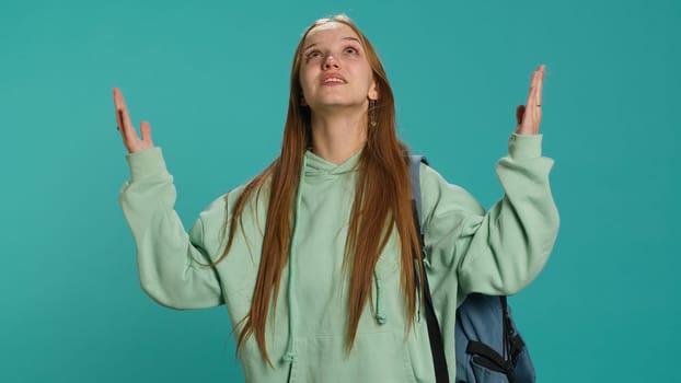 Pious woman looking up towards sky, waiting for sign from god. Spiritual girl doing worship hand gesturing, spreading arms, hoping for miracle, studio background, camera A