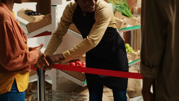 Local merchant opening grocery store doors and welcoming clients, greeting people with new organic homegrown fruits and vegetables. African american vendor selling eco friendly food items. Camera 1.