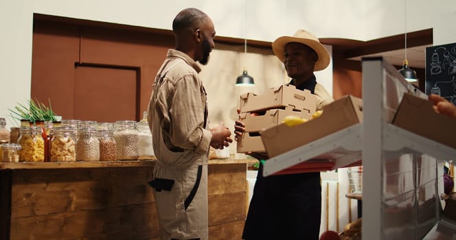 African american supplier bringing crates filled with eco fruits, local vendor at farmers market receiving freshly harvested produce. Contractor restocking natural food alternatives. Camera 2.