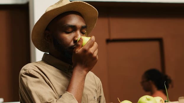 Male customer enjoying fresh smell of green apples in crates, choosing to buy fruits and veggies from local zero waste eco store. Young adult smelling natural organic aroma of produce. Camera 1.