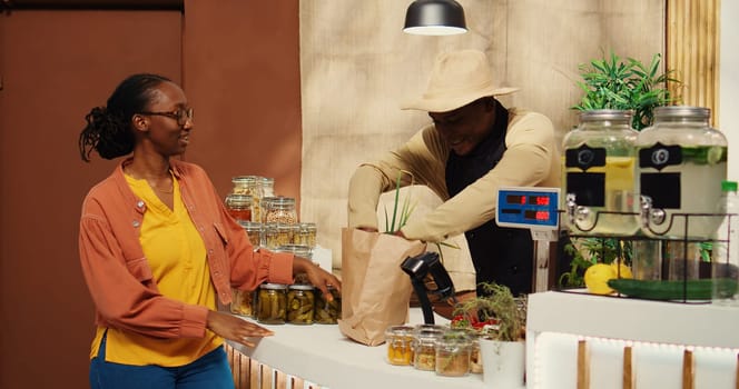 African american vendor weighting produce for regular client at supermarket cash register, using electronic scale to sell locally grown goods. Buyer supporting local farming business. Camera 2.