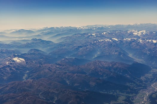 Beautiful view of the rocky dark tops of the Alpine mountains in places with snow from the window of a flying airplane over Switzerland, close-up side view.