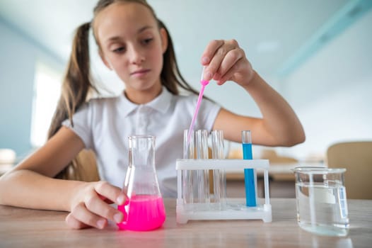 A schoolgirl conducts experiments in a chemistry lesson. Girl pouring colored liquids from a beaker