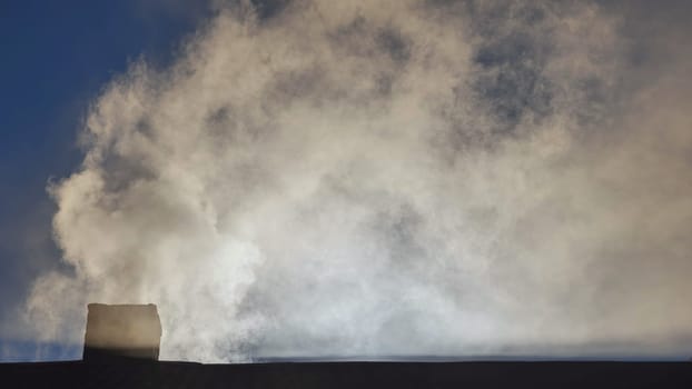 Silhouette of smoke against the sun from the chimney of a village house