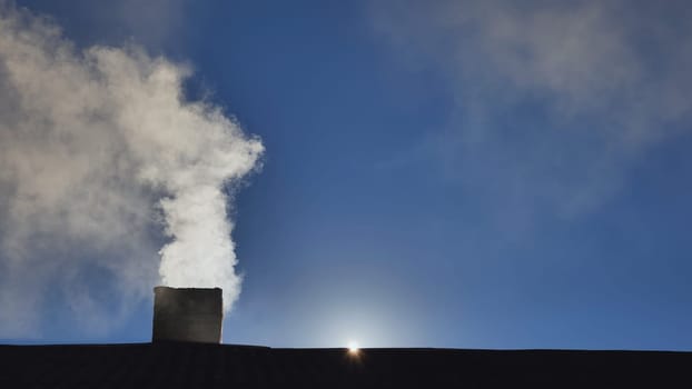 Silhouette of smoke against the sun from the chimney of a village house