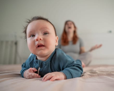 A three-month-old boy lies on his stomach on the bed and his mother sits behind him and cries. Postpartum depression