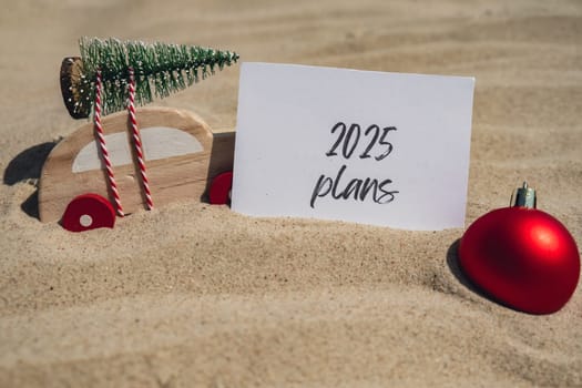 2025 PLANS text on paper greeting card on background sandy beach sun coast. Christmas balls Santa hat New Year New Me Resolutions decoration. Summer vacation decor. Holiday concept calendar date postcard. Getting away Travel Business concept