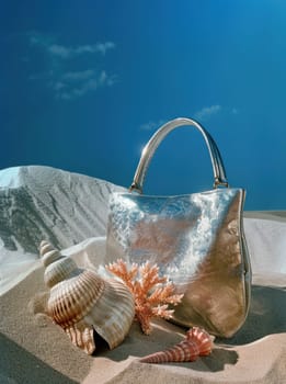 Fashionable silver purse and seashells on sandy beach with blue sky background as travel and beauty concept