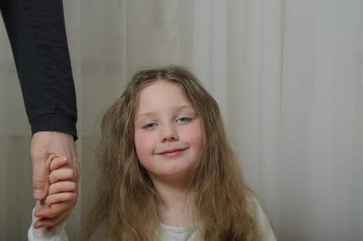 A little girl is holding the hand of an adult. Portrait of a child with long blond hair and blue eyes. Hand of an adult wearing a black long sleeve. man. fater.
