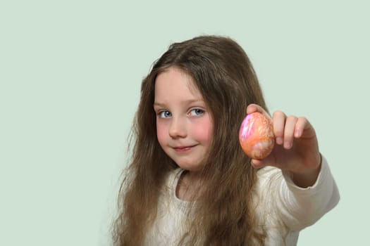 A little girl shows an Easter egg. Isolate. A child with long blond hair and blue eyes. She is holding an egg in her outstretched hand.