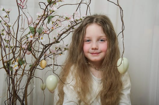 Flowering branches decorated with Easter eggs and a girl. A little girl of 5-6 years old with long, blond hair and blue eyes.