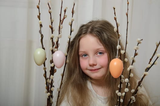 Willow branches with Easter eggs and a girl. A little girl of 5-6 years old with long, blond hair and blue eyes.