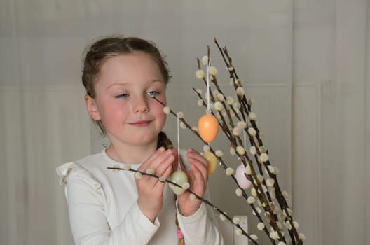 Willow branches with Easter eggs and a girl. A little girl of 5-6 years old with long, blond hair and blue eyes.