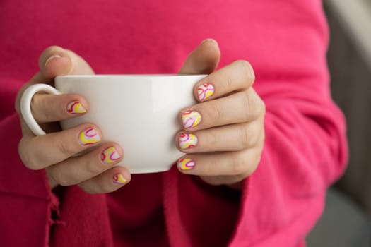 Stylish colorful summer female nails holding white cup of coffee or tea. Modern trendy stylish Beautiful manicure. Cute pastel nail minimalistic design concept of beauty treatment. Gel nails. Skin care. Beautician