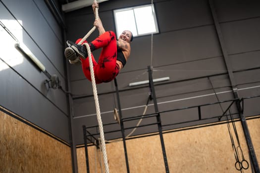 Low angle view photo of a happy woman climbing a rope exercising in a cross training center