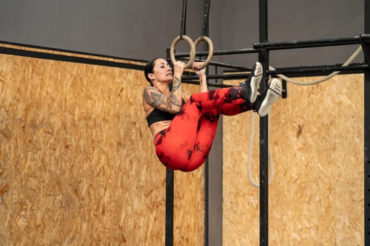 Strong aged woman training using olympic rings alone in a gym