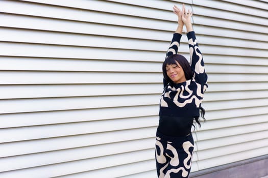 Sensual urban dancer performing raising hands in street next to urban metallic wall