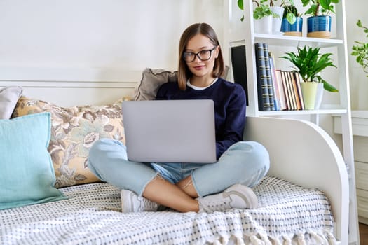 Young woman in glasses working at home, sitting on couch using laptop computer. Freelancing, training, education, remote work, leisure, internet online technology applications apps concept