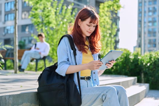 Young attractive female college student using digital tablet outdoor, educational building background. Education, technology, training, 19,20 years age youth concept