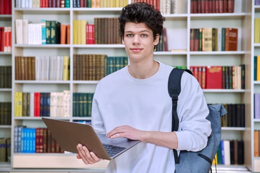 Portrait of handsome serious confident smart young male student with laptop computer in educational building in library. Education internet technology e-learning, learning services applications, youth