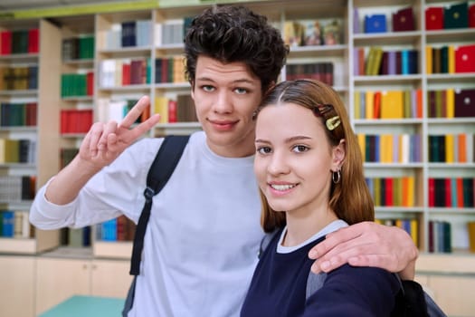 Selfie portrait of friends teenagers high school students looking at camera inside classroom. Having fun laughing teenage guy and girl in library. Friendship adolescence education lifestyle