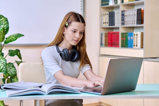 Teenage girl student studying in the high school library. Education, adolescence, knowledge concept