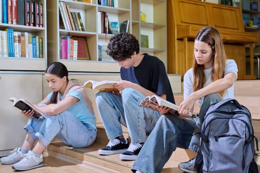 Teenage students sitting in college high school library reading books. Education, training, adolescence and youth concept