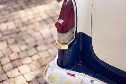 Close-up of a vintage car's tail light parked on a cobbled street, highlighting its classic aesthetic.