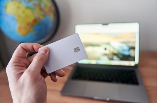 A person is holding a credit card in front of a personal computer with a laptop screen. They are using the touchpad to make a gesture