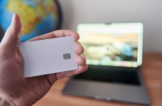 A person is holding a credit card in front of a personal computer with a laptop screen. They are using the touchpad to make a gesture