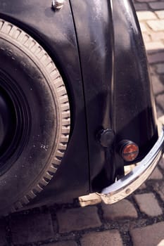 Close-up of a vintage car's tail light parked on a cobbled street, highlighting its classic aesthetic.