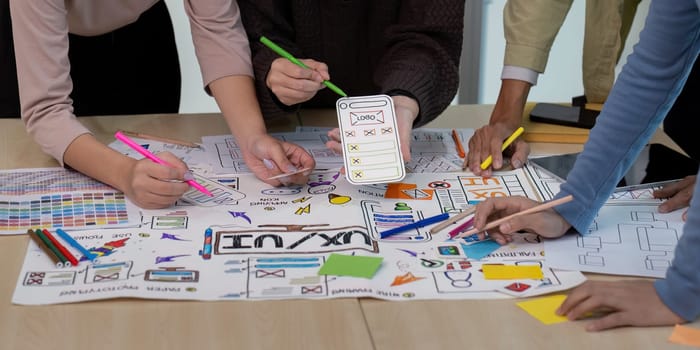 A group of UX developers and UI designers brainstorming with sketches, wireframes, and colorful markers on a table, showcasing the creative process of designing user interfaces.