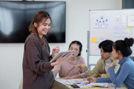 Team of UX developers and UI designers collaborating in a modern office, using a digital tablet and whiteboard for brainstorming ideas.