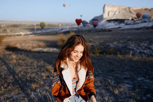 Serene woman in denim outfit gazes at colorful hot air balloons floating in a peaceful field