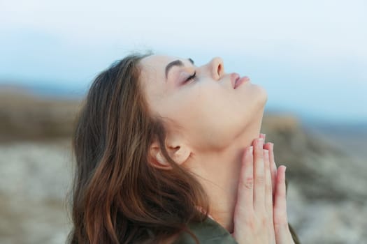 Woman standing peacefully with eyes closed, hands on chest, looking up at the sky in contemplation