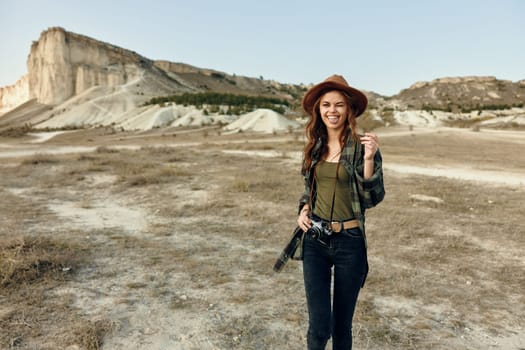 Woman in hat capturing desert landscape with camera and mountains in background