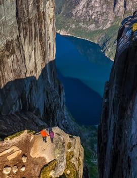 Kjeragbolten, Norway, Two figures stand on a narrow ledge overlooking a dramatic Norwegian fjord. a couple of men and women visiting Kjeragbolten, Norway