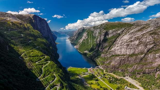An aerial view of a winding road snaking through the dramatic, green cliffs of a Norwegian fjord on a bright, sunny day. Kjerag, Lysebotn, Lysefjorden, Norway