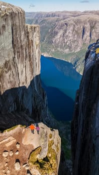 Two hikers stand on the edge of Kjeragbolten, Norway, a dramatic cliff in Norway, overlooking a stunning blue fjord. a couple of men and women visiting Kjeragbolten, Norway