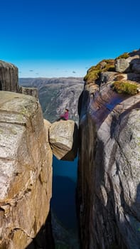 A person sits on the edge of Pulpit Rock in Norway, gazing out over the breathtaking landscape. The sheer drop-off and dramatic rock formations offer a stunning visual contrast to Kjergabolten Norway