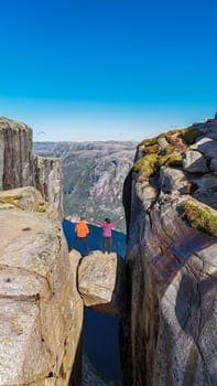 Two people stand on the edge of Kjeragbolten, a famous cliff in Norway, looking out at the breathtaking view of the surrounding landscape. a couple of men and women visiting Kjeragbolten